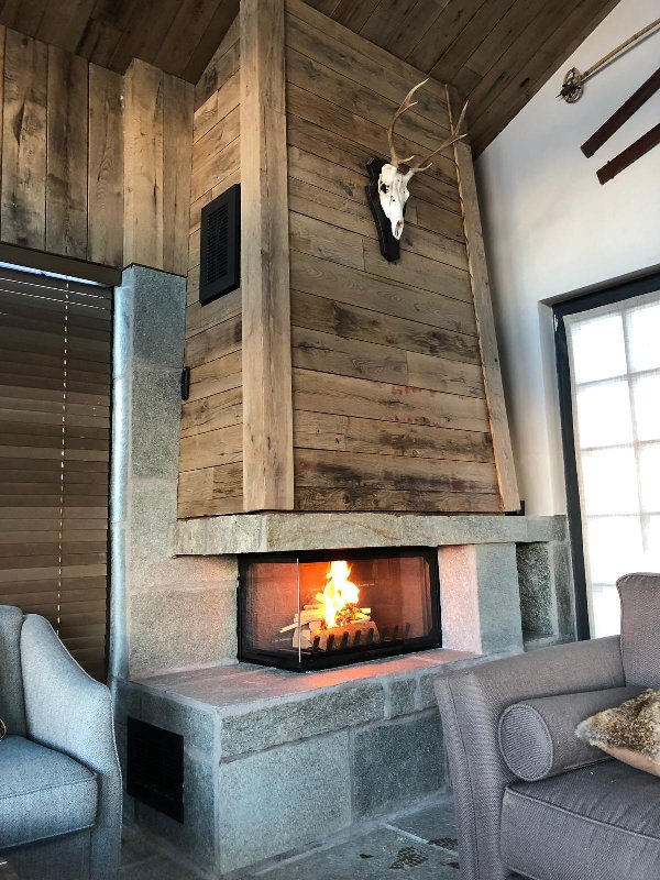 Cheminée vitre latérale avec un socle en pierre et un revêtement en bois - Carron-Lugon